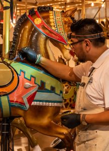 An artist touches up the paint one one of the carousel horses